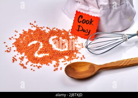 Konzept für den Kochtag. Linsenstapel in Form der Zahl 20. Holzlöffel und Mischwerkzeug auf weißem Hintergrund. Stockfoto