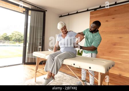 afroamerikanischer männlicher Physiotherapeut, der kaukasischen älteren Frau zu Hause eine Massage zurückgibt Stockfoto