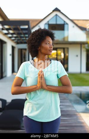 afroamerikanische junge Frau, die Yoga praktiziert und in der Nähe des Pools meditiert Stockfoto