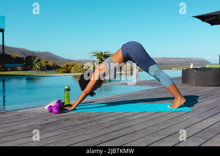 afroamerikanische junge Frau, die im Freien in der Nähe des Pools Yoga praktiziert Stockfoto
