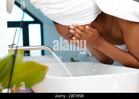 Nahaufnahme einer afroamerikanischen Frau, die sich zu Hause im Waschbecken das Gesicht wusch Stockfoto