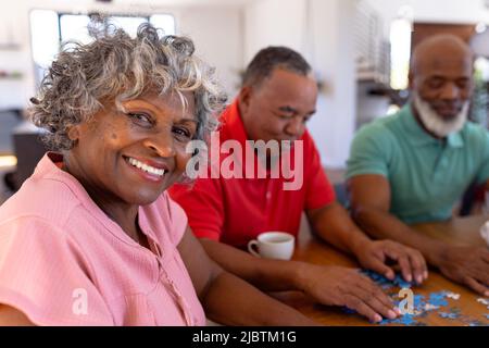 Porträt einer lächelnden, multirassischen älteren Frau, die Puzzle mit männlichen Freunden im Pflegeheim löst Stockfoto