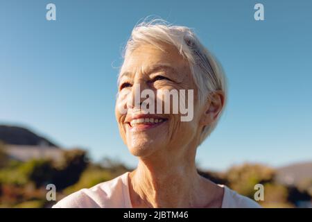 Nahaufnahme einer fröhlichen asiatischen älteren Frau mit kurzen Haaren, die auf den klaren blauen Himmel im Hof blickt Stockfoto