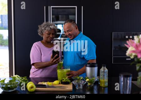 afroamerikanische ältere Frau zeigt dem kaukasischen Mann in der Küche im Altersheim ein Mobiltelefon Stockfoto