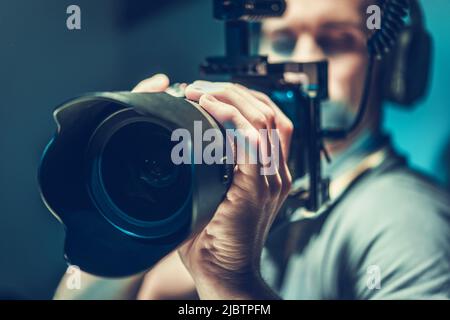 Der männliche Videograf konzentrierte sich auf die Aufzeichnung der Aufnahmen mit seiner Mirrorless Camera. Digital Videography Industry Theme. Stockfoto