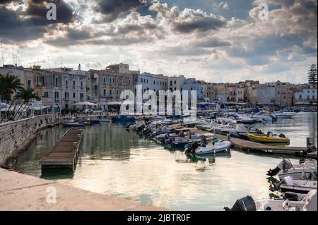 Trani, Apulien, Italien. August 2021. Schöner Blick auf den Yachthafen, umgeben von Häusern mit farbigen Fassaden, dramatischer Himmel mit Lichtstrahlen, die t filtern Stockfoto