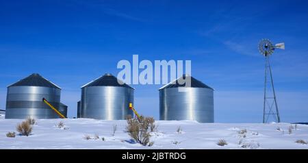 Windmühle und Stahlkornsilos im Winterschnee mit blauem Himmel auf dem Bauernhof für die landwirtschaftliche Landwirtschaft Stockfoto