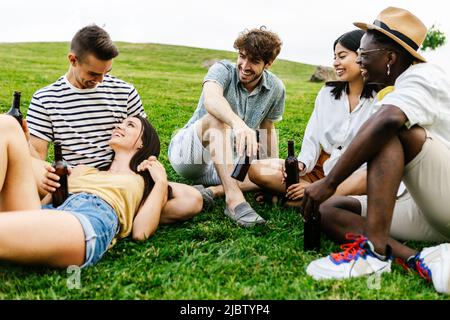 Eine Gruppe von multirassischen Freunden, die im öffentlichen Park draußen rumhängen und sich unterhalten Stockfoto