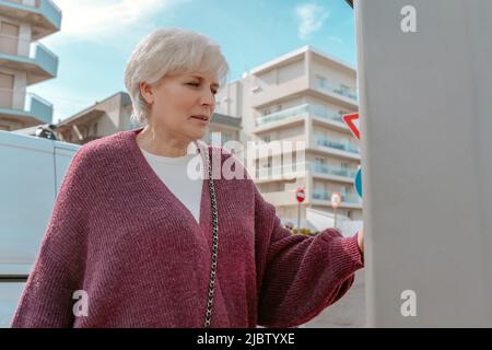 Fokussierte ältere Frau, die an der Tankstelle steht Stockfoto