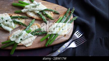 Spargel und Käse-Bruschetta auf Holzschneidebrett. Direkt darüber. Gesunde Ernährung. Stockfoto