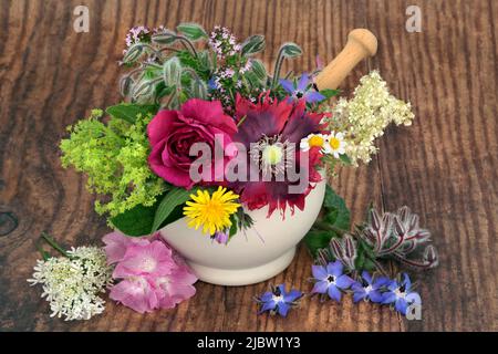 Kräuterblütenmedizin mit essbaren Blumen und Kräutern in einem Mörser auf rustikalem Holz. Alternative Naturheilmittel auf pflanzlicher Basis. Natürliche Gesundheitsfürsorge. Stockfoto