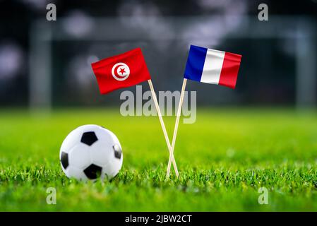 Tunesien vs. Frankreich, Bildungsstadt, Fußballspiel-Tapete, Handgefertigte Nationalflaggen und Fußball auf grünem Gras. Fußballstadion im Hintergrund. Stockfoto