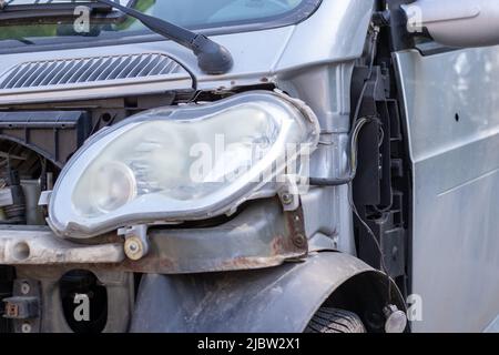 Defekte Scheinwerfer infolge einer Kollision. Gebrochenes graues Auto nach einem Unfall. Konzept eines Autounfalls. Notscheinwerfer, Motorhaube und Stoßfänger beschädigt. D Stockfoto