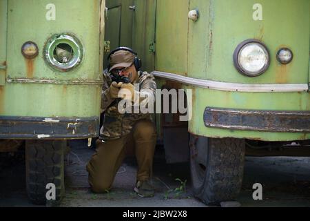 Militärmann versteckt sich in Position zwischen alten rostigen Bussen mit Waffe in den Händen. Shooter mit Pistole vorbereitet zu schießen. Ranger während der Militäroperation. Kampftrainingssoldat der Spezialeinheiten. Stockfoto