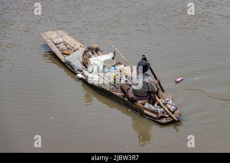 Ein armer Mensch schwimmt auf einem alten Boot voller recycelter Materialien Stockfoto