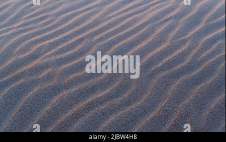 Sand kräuselt Textur mit Wellen bei Sonnenuntergang als Hintergrund oder Tapete. Stockfoto