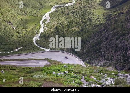 Blick auf Serpentinenstraße auf Bergpass und wunderschöne alpenlandschaft. Der Motorradfahrer auf der Kurve oben mit dem grünen Sommertal des Flusses. F Stockfoto