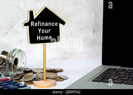 Refinanzieren Sie Ihren Home-Text auf Holzhausmodell mit verschwommenem Glas von Münzen, Rechner und Notizbuch Hintergrund. Immobilien Hypothek und Darlehen Konzept. Stockfoto