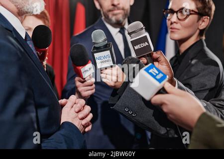 Nahaufnahme einer Gruppe von Journalisten, die Mikrofone vor dem Geschäftsmann halten und ihn auf der Konferenz interviewen Stockfoto