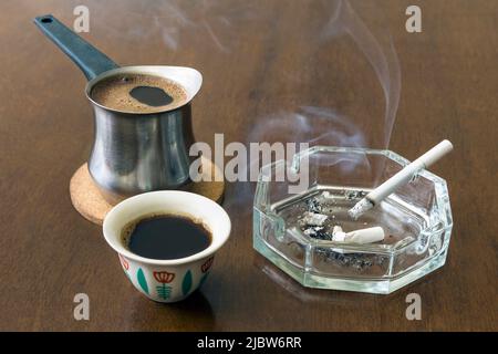 Traditionelle libanesische Kaffeebecher mit Aschenbecher und Zigarette auf einem Holztisch Stockfoto