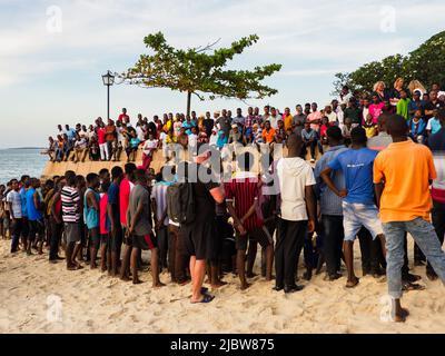 Stone Town, Sansibar, Tansania - Januar 2021: Menschenmassen beobachten, wie junge Menschen auf einem Innenrohr an einem Sandstrand in Stone Town springen. Afrika Stockfoto