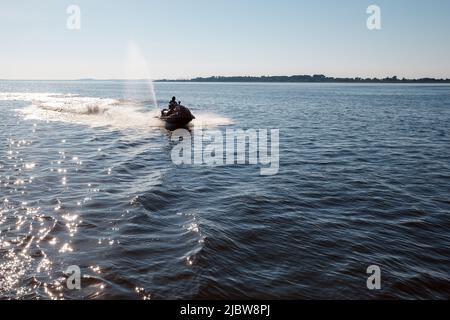 Mittags springt die Silhouette eines starken Mannes auf den Jetski über dem Wasser Stockfoto