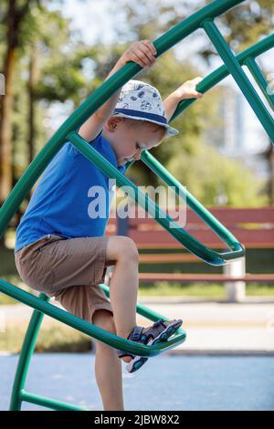 Kleiner Junge sehr konzentriert klettern auf den U-Bahnleitern in der Stadt Spielplatz. Stockfoto