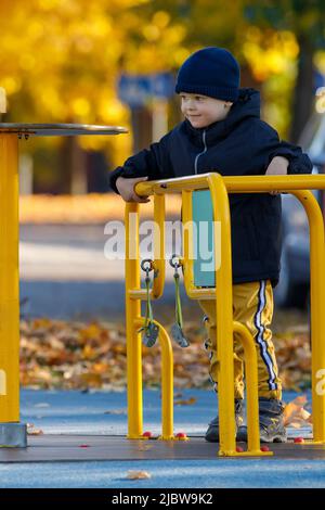 Der Junge dreht sich auf dem Karussell auf dem Spielplatz. Kreisförmige gelbe Drehbewegung aus Metall. Stockfoto