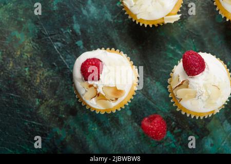Leichtes köstliches Dessert - Muffins mit Rahm, frischen Himbeeren und Mandelflocken. Isoliert auf einem dunkelgrünen Hintergrund. Blick von oben. Geburtstag, ann Stockfoto