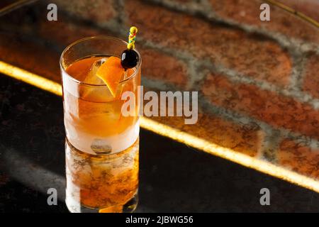 Kristallglas mit strahlend kalten alkoholischen Cocktails, dekoriert mit orangefarbener Schale. Unscharfer Hintergrund. Negroni-Cocktail Stockfoto