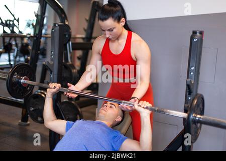 Der junge Personal Trainer hilft beim Training mit Bankdrücken Stockfoto