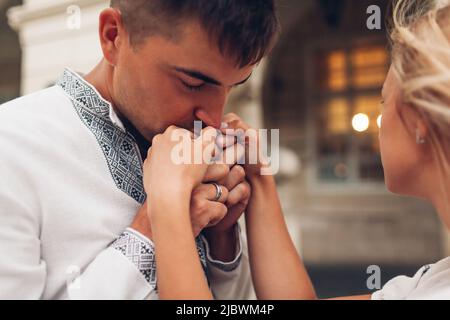 Junger Mann in der Liebe küsst die Hände seiner Frau. Pärchen, die im Freien in traditionellen ukrainischen Hemden spazieren gehen. Nahaufnahme Stockfoto