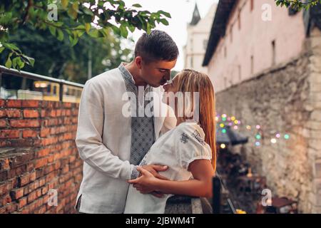 Liebevolles Paar, das in der Altstadt von Lviv in traditionellen ukrainischen Hemden herumläuft. Die Menschen umarmen sich entspannt durch Arsenal unter Regen Stockfoto