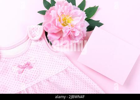 Rosa Baby Mädchen Kleidung und Pfingstrose Blume auf rosa Hintergrund. Babygeburtstag, Einladung oder Grußkarte. Speicherplatz kopieren. Flach liegend. Stockfoto