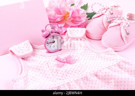 Rosa Baby Mädchen Kleidung und Pfingstrose Blume auf rosa Hintergrund. Babygeburtstag, Einladung oder Grußkarte. Speicherplatz kopieren. Flach liegend. Stockfoto