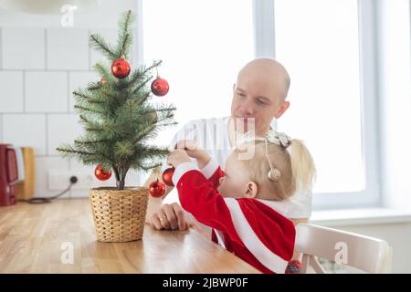 Vater mit Kleinkind Tochter mit Cochlea Implantate Spaß im weihnachtswohnzimmer - Einbeziehung und innovative Behandlung für Taubheit mit Stockfoto