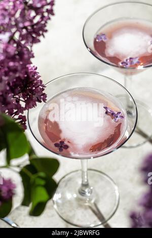 Zwei frische Rosé-Weingläser mit Fliederblumen und Schatten auf grauem Hintergrund, Nahaufnahme, Draufsicht. Sommergetränk für Party oder Weinladen oder Verkostung c Stockfoto