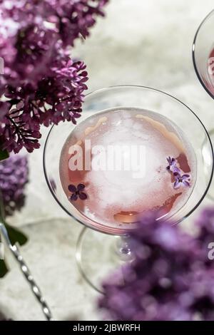 Rosenchampagner im Glas mit Fliederblüten auf grauem Hintergrund, Nahaufnahme. Sommerdrink für Party, Weinladen oder Verkostungskonzept Stockfoto
