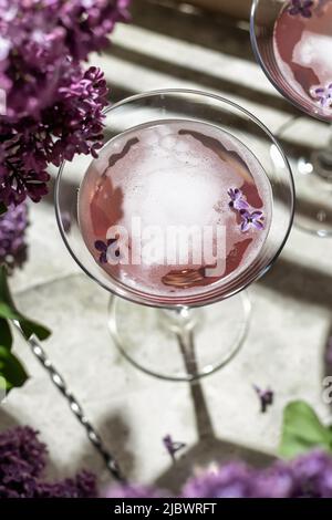 Roséwein im Glas mit Fliederblumen und Schatten auf grauem Hintergrund, Nahaufnahme, Draufsicht. Sommerdrink für Party, Weinladen oder Verkostungskonzept Stockfoto