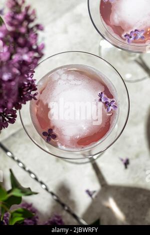 Rosé- oder Sektgläser mit Fliederblüten und Schatten auf grauem Hintergrund, Nahaufnahme, Draufsicht. Sommerdrink für Party, Weinladen oder Verkostung Co Stockfoto