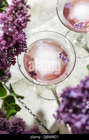 Frische Rosé-Weingläser mit Fliederblumen und Schatten auf grauem Hintergrund, Nahaufnahme, Draufsicht. Sommerdrink für Party, Weinladen oder Verkostung Conce Stockfoto