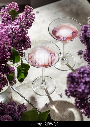 Zwei Roséweingläser mit Fliederblumen und Schatten auf grauem Hintergrund. Sommerdrink für Party, Weinladen, Menü oder Verkostungskonzept Stockfoto