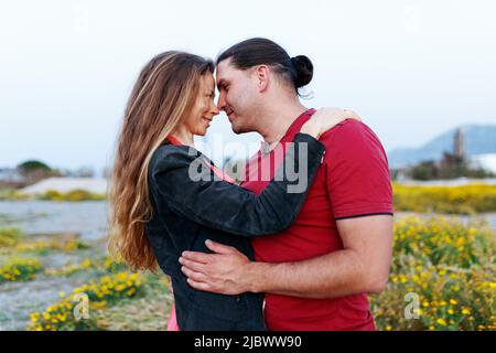 Porträt eines hübschen Paares mittleren Alters, das sich anschaut und umarmt, während es im Sommerpark auf Gras steht. Stockfoto