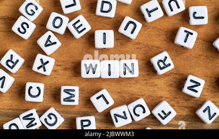 Kleine weiße und schwarze Perlenwürfel auf Holzbrett, Buchstaben in der Mitte buchstabieren GEWINNEN Stockfoto