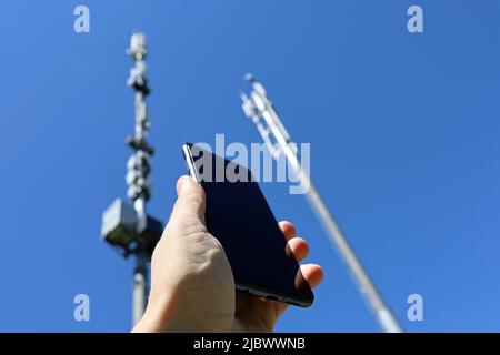 Männliche Hand mit Smartphone auf dem Hintergrund von Zelltürmen. Mobilkommunikationsgeräte, Signalstärke des Telefons Stockfoto