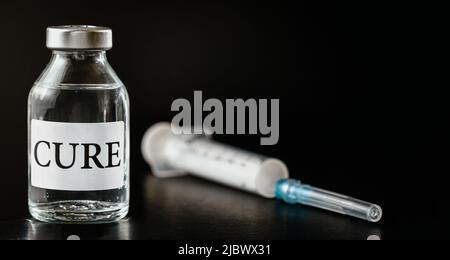 Glas-Impfstofffläschchen mit Etikett Cure auf schwarzem Brett, hypodermische Spritze in der Nähe Stockfoto