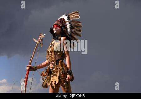 Eine indianische Ureinwohnerin steht vor grauen Regenwolken. Sie trägt einen gefiederten Kopfschmuck und trägt traditionelle indische Kleidung. Stockfoto