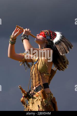 Eine indianische Ureinwohnerin steht vor grauen Regenwolken. Sie trägt einen gefiederten Kopfschmuck und trägt traditionelle indische Kleidung. Stockfoto