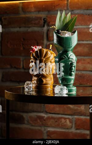 Tiki Getränke Cocktails. Zwei Cocktails in verschiedenen Gläsern vor dem Hintergrund einer Bar, die mit Trockenfrüchten und tropischen Blättern dekoriert ist Stockfoto