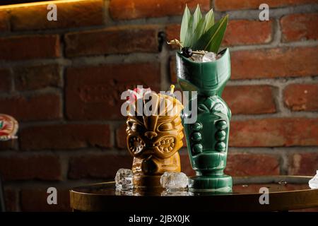 Tiki Getränke Cocktails. Zwei Cocktails in verschiedenen Gläsern vor dem Hintergrund einer Bar, die mit Trockenfrüchten und tropischen Blättern dekoriert ist Stockfoto